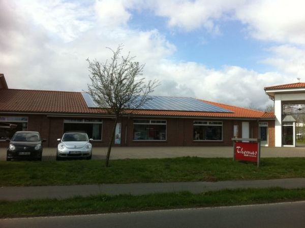 Flaches Firmengebäude mit Solaranlage auf dem Dach, davor Autos und ein Werbeschild.