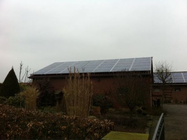 Photovoltaikanlage mit Solarmodulen auf dem Dach eines Hauses in einem Gartenbereich.