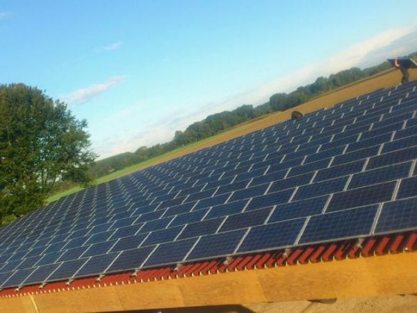 Große Photovoltaikanlage mit Solarmodulen auf einem Dach in ländlicher Umgebung.
