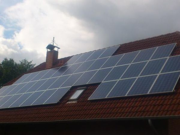 Photovoltaikanlage mit Solarmodulen auf einem roten Ziegeldach unter bewölktem Himmel.